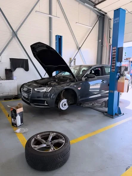 Audi A4 gri în atelier, cu capota deschisă și roata față demontată